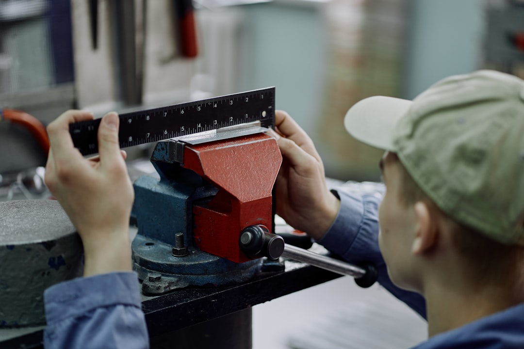 A worker measures a metal piece clamped in a vise.