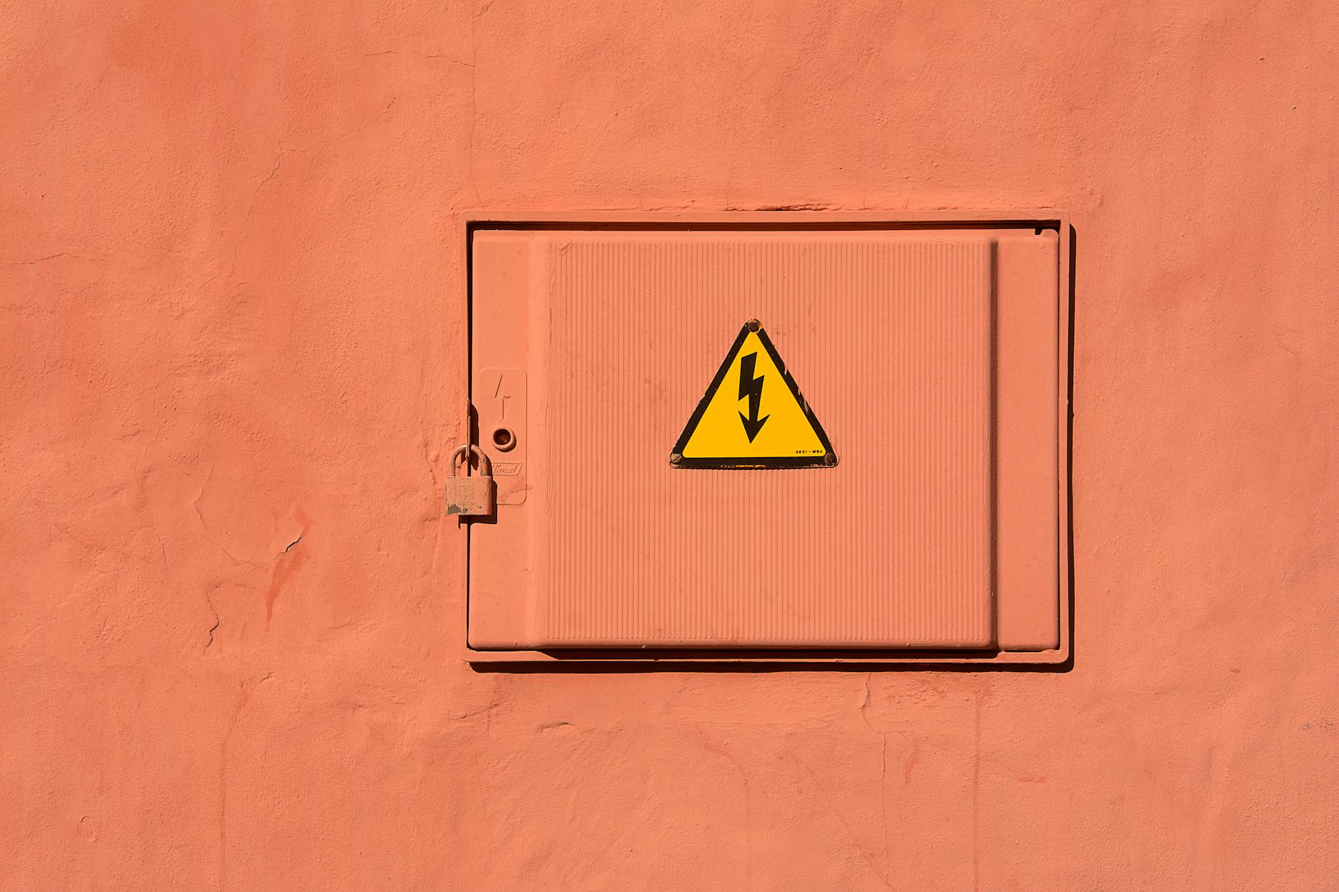 Bright yellow high voltage warning sign on a locked electrical box.