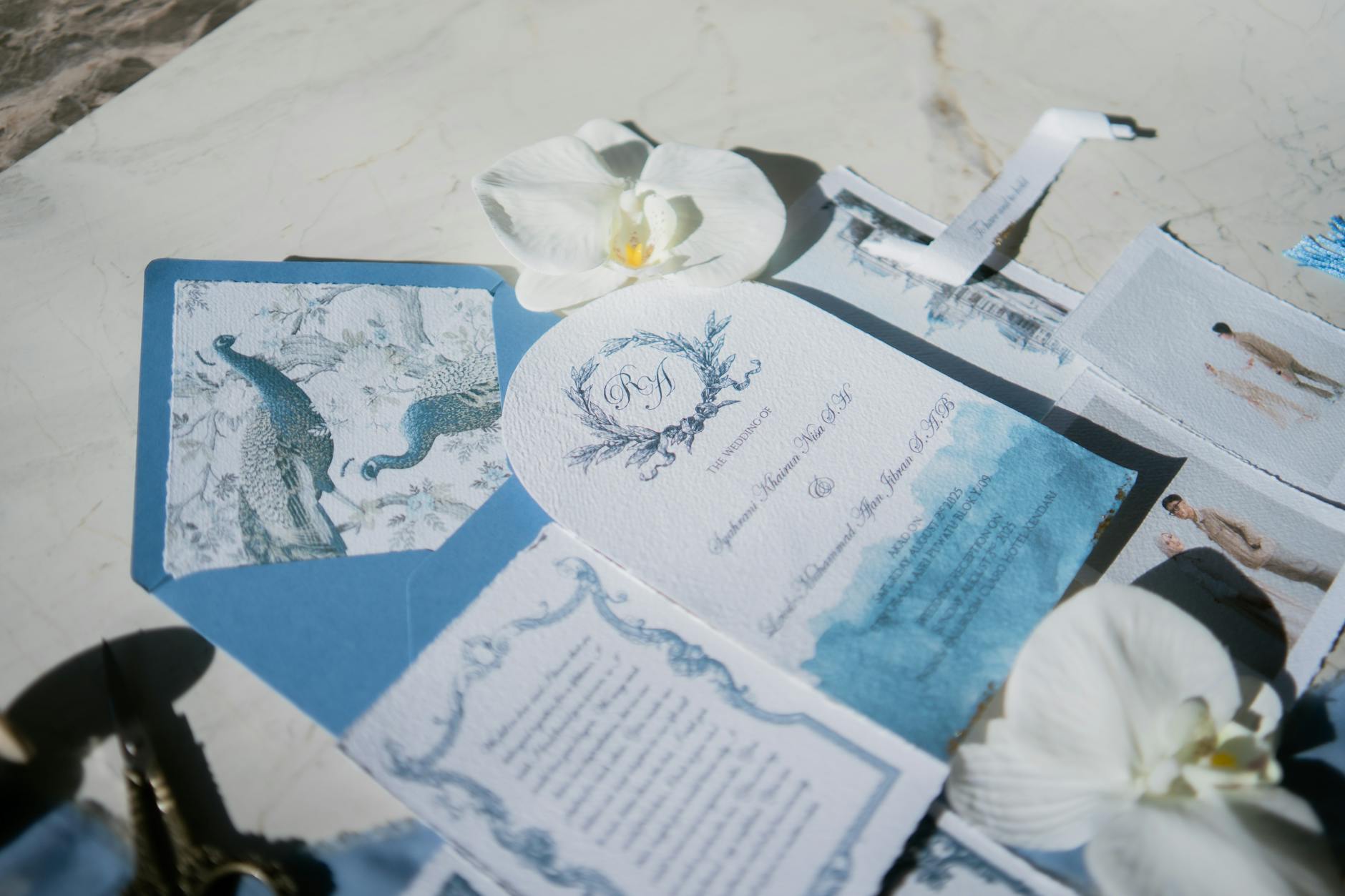 Elegant wedding invitation set featuring peacock design and white orchids on a marble background.