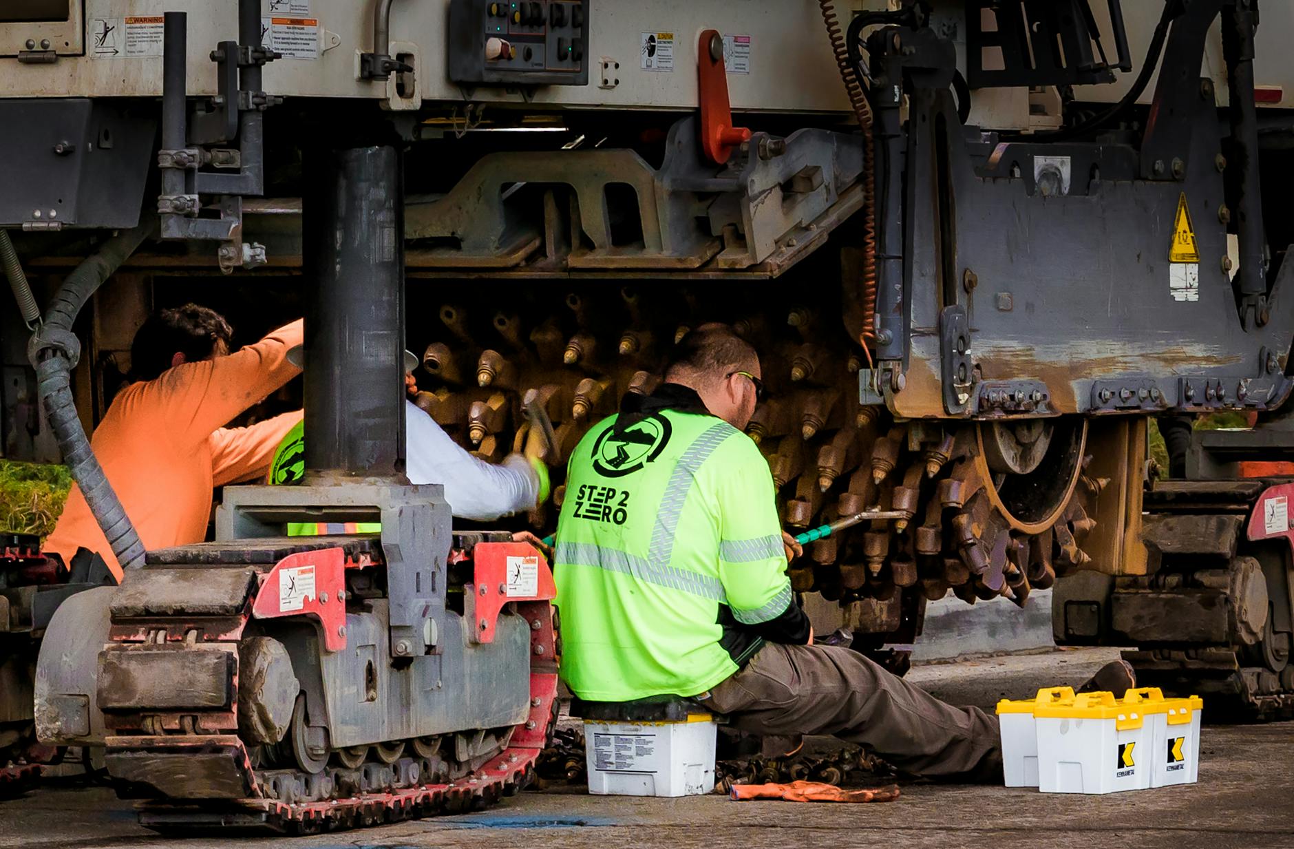Engineers performing maintenance on construction equipment in an industrial workshop setting.