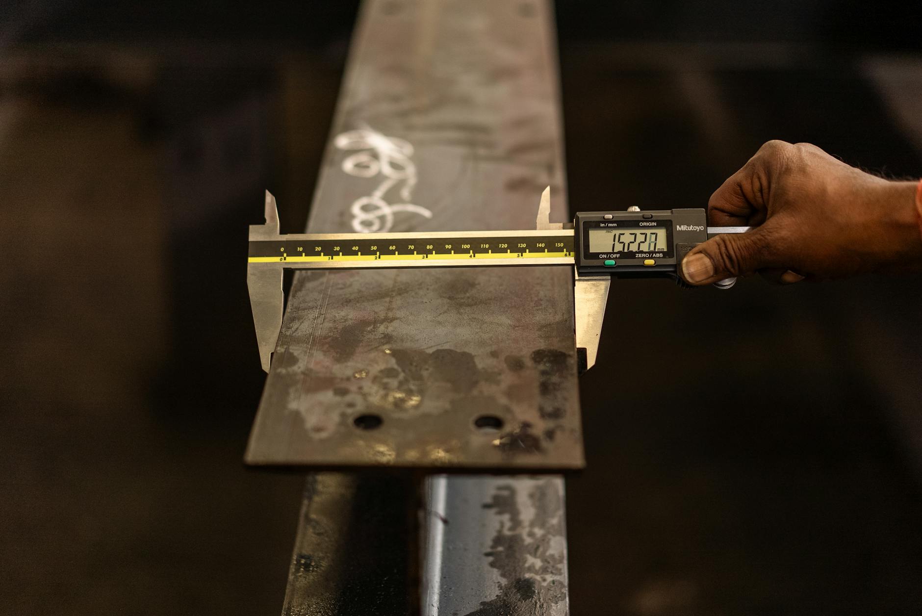 Close-up of a worker measuring a steel beam with a digital caliper in industrial inspection
