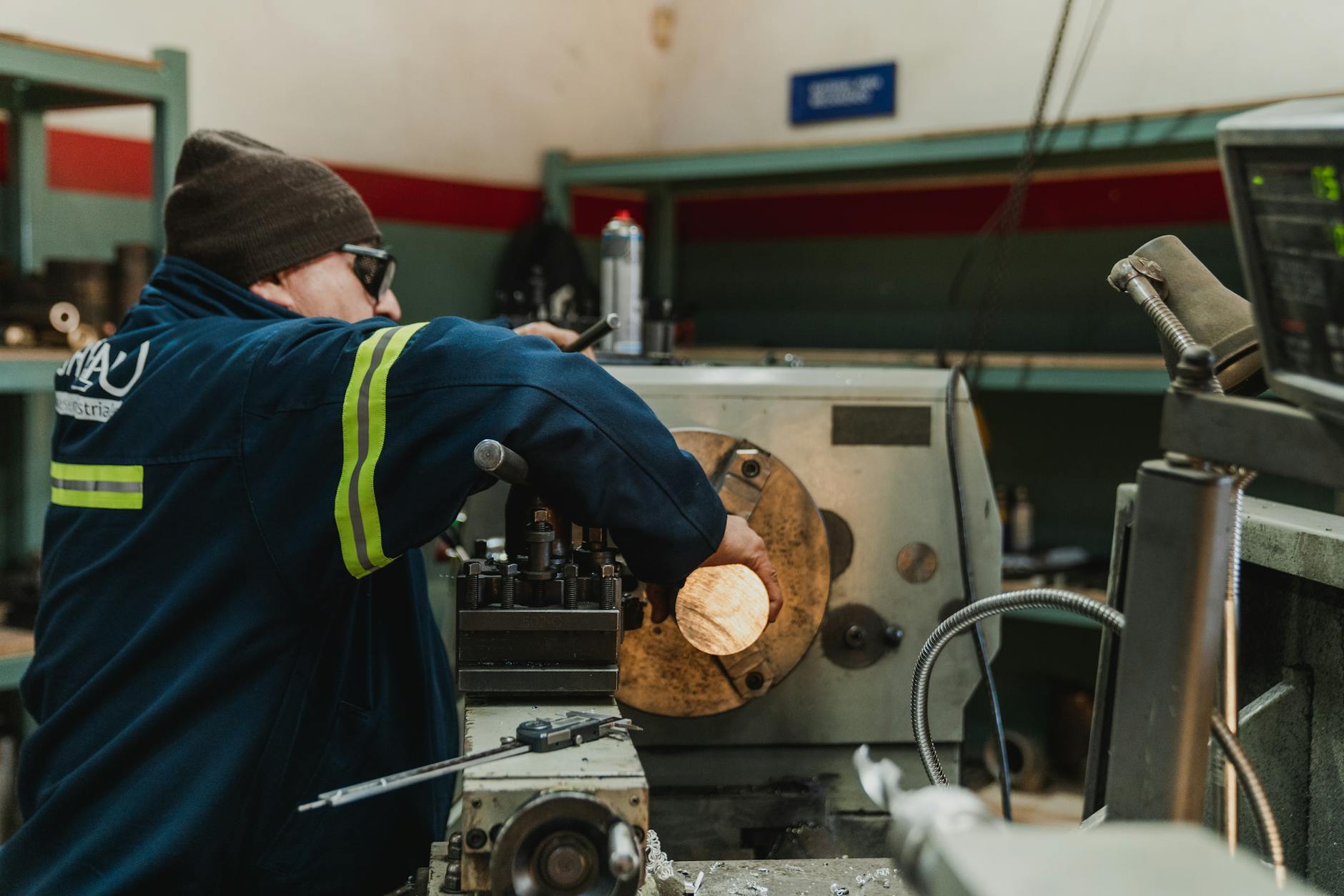 Industrial worker focused on operating a lathe in a busy workshop setting.