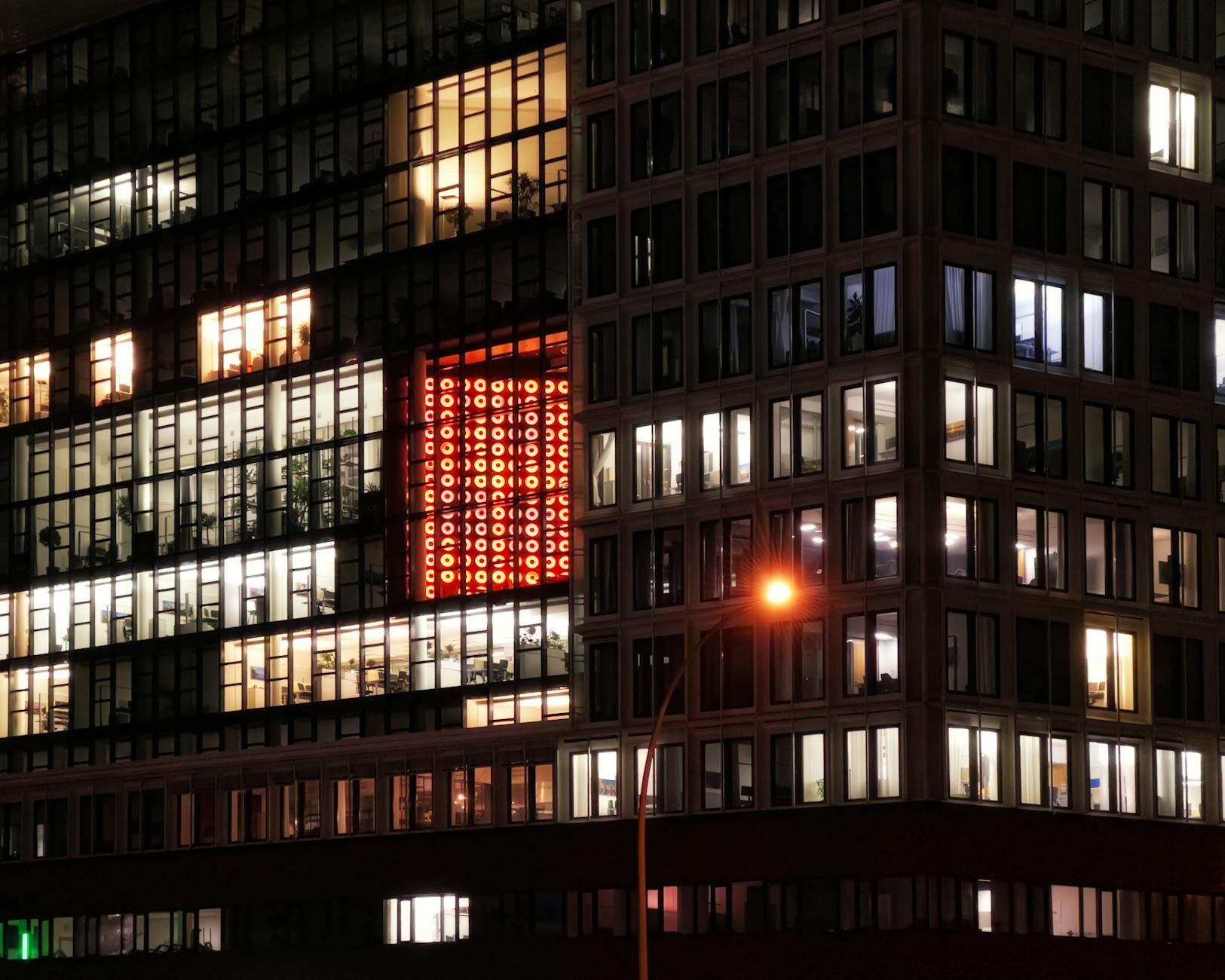 Night view of an urban building with illuminated windows and a distinctive red sign. Perfect for cityscape and architect