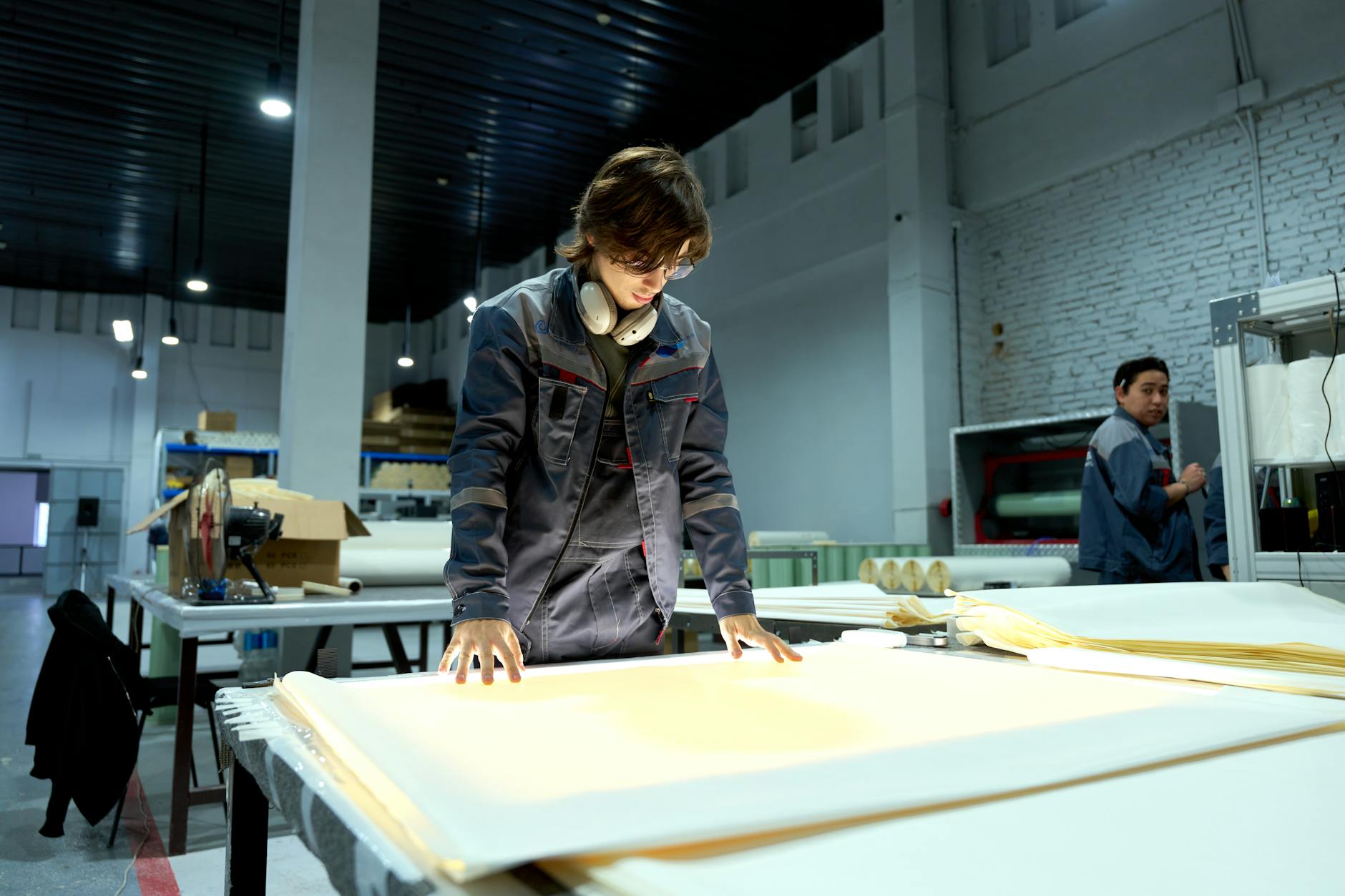 Worker in uniform examining sheets in a brightly lit factory environment for quality control