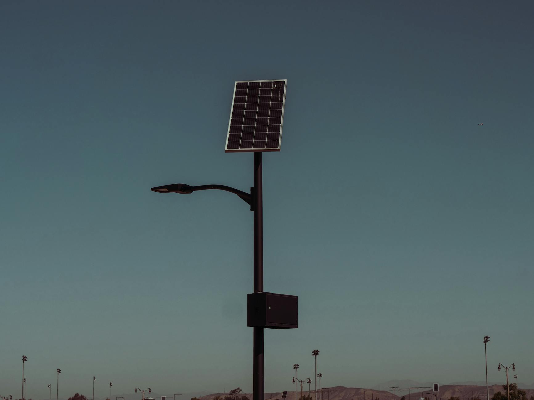 Street light with solar panel against a dusky sky, symbolizing renewable energy.